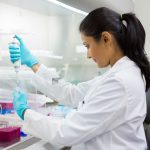 Closeup portrait, scientist pipetting from 50 mL conical tube with blue liquid solution, performing laboratory experiments, isolated lab . Forensics, genetics, microbiology, biochemistry